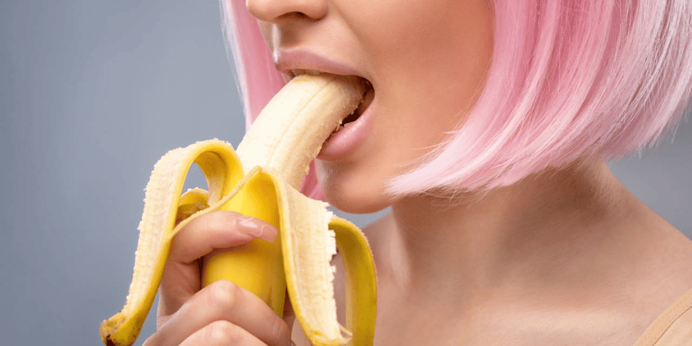 consejos-para-dar-un-buen-sexo-oral-y-dejar-a-tu-pareja-boquiabierto-chica-de-cabello-rosado-comiendo-banana-mejoresjuguetessexuales.com